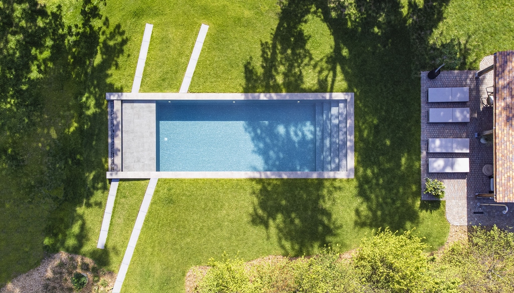 Bovenaanzicht van een rechthoekig zwembad met keramische tegels als zwembadrand en een poolhouse.